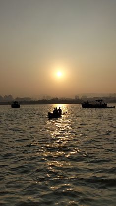 three boats floating on top of a large body of water under a sun set sky