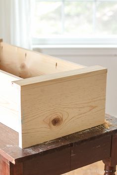 an empty wooden box sitting on top of a table next to a window in a room