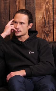 a young man sitting on top of a couch talking on a cell phone while wearing a black hoodie