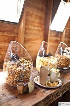 three glass containers filled with popcorn on top of a wooden table next to cups and saucers