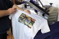 a man holding up a t - shirt with pictures on it in front of a printer