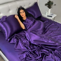 a woman laying on top of a bed covered in purple sheets and pillows with her hand under the pillow