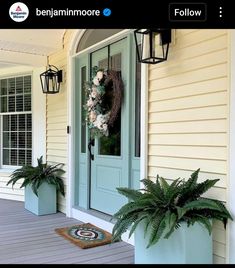 a front porch with two planters and a wreath on the door sill next to it