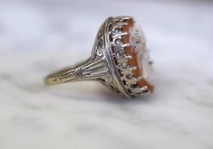 Metal: 14kt White Gold Stone: Orange Shell Approximate Measurements Of Cameo: 16x12 mm Shape: Oval Weight of entire piece with stones: 6.10 grams Length Of Center Part Of Ring: 20.29 mm Width Of Center Part Of Ring: 16.11 mm Height Of Ring From Top To Bottom: 27.64 mm Width Of Shoulders: 8.35 mm Ring Size: 7 Sizable: Yes. Please state in note to seller box at checkout or message us. Age: Vintage, approximately 1950's. Antique Orange Oval Ring, Vintage Orange Rings For Collectors, White Cameo Collectible Rings, Unique Orange Cabochon Ring, Vintage Orange Cabochon Rings, Amethyst And Diamond Ring, Cameo Ring, Gold Dipped, Orange Gold