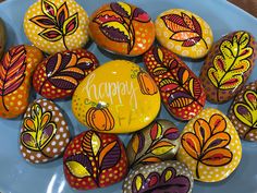 painted rocks with the words happy written on them are arranged in a blue bowl and decorated with autumn leaves