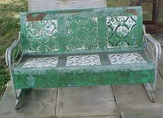 a green metal bench sitting on top of a sidewalk