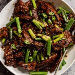 a white bowl filled with meat and green beans on top of a table next to a fork