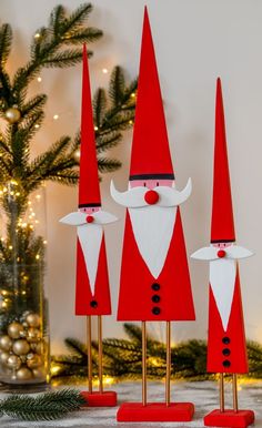 three red and white gnomes standing next to a christmas tree