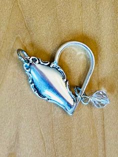 a silver teapot shaped like a heart on a wooden surface with a hook in the middle