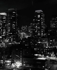 black and white photograph of city skyline at night with heart shaped object in the sky