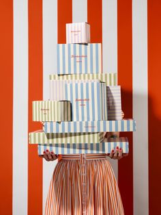 a woman holding several boxes in front of her face and wearing an orange striped dress