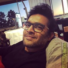 a man with glasses sitting in an airport terminal next to an elephant and looking at the camera