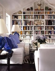 a living room filled with white furniture and lots of bookshelves full of books