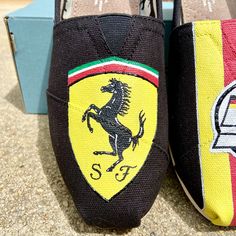 "This was a YourChoice - Custom design completed in August of 2020 on a Women's size 7 with a base-color of black. The buyer requested a mixed pair, one shoe showing the Ferrari crest and the other shoe with a German flag stripe down the center, continuing to the back of the heel, with the number \"5\" on the front.  The design can be replicated on the color of your choice. Additional embellishments by request include rhinestones, extra or less glitter, wording/personalization etc. Each pair wit Black Casual Custom Sneakers With Embroidered Logo, Casual Black Custom Sneakers With Embroidered Logo, Color Complementary, German Flag, Design Shoes, Number 5, Shoe Show, New Me, Base Colour