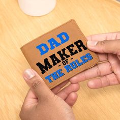 a hand holding a leather wallet that says dad maker of the rules in blue on it