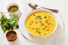 a white plate topped with a bowl of soup next to two small bowls of seasoning