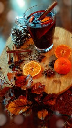 a cup of mulled with oranges and cinnamon on a wooden tray surrounded by autumn leaves