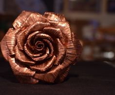 a rose made out of copper foil sitting on top of a table