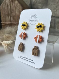 three pairs of earrings on display in front of a piece of paper with an image of the sun and two fish