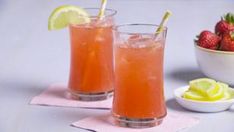 two glasses filled with drinks next to a bowl of strawberries