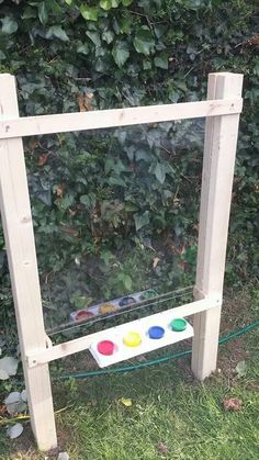 an easel with paint on it in front of a bush and fenced area