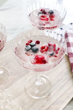 two glasses filled with ice and berries on top of a wooden table next to a red white and blue napkin