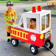 two children in fireman costumes are riding on a toy truck with a fireman's hat