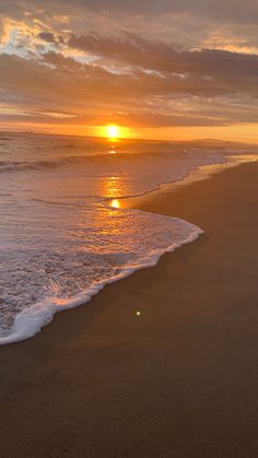 the sun is setting over the ocean with waves lapping in front of it,