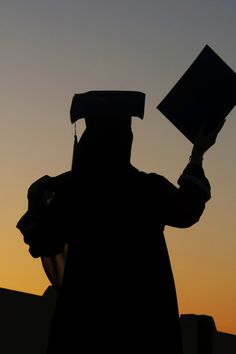 the silhouette of a person wearing a graduation gown and holding a book in their hand