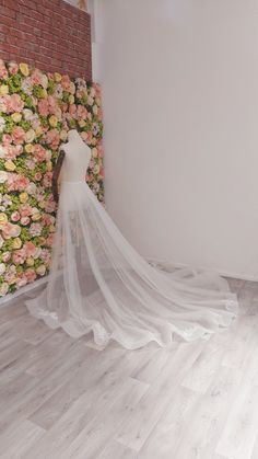 a white wedding dress is on display in front of a floral wall with pink and yellow flowers