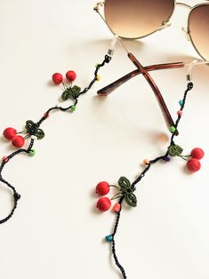 This eyeglass holder strap is made of crocheted cherries and decorated with beads in different colors. It is light weight and measures approx 28”.  #eyeglasses #eyeglassholder #eyeglasschain #glasses #glasseschain #sunglassholder #readers #booklovers #giftformom #giftforher #mothersday #motherdaygifts #mothersdayideas Handmade Glasses Chains For Summer Party, Handmade Summer Party Glasses Chains, Summer Beaded Chain Glasses Chains As Gift, Summer Beaded Glasses Chain Gift, Gift Plastic Glasses Chains With Adjustable Chain, Trendy Green Glasses Chains For Beach, Black Glasses Chains For Summer Beach, Summer Gift Black Glasses Chains, Red Glass Glasses Chains For Gift