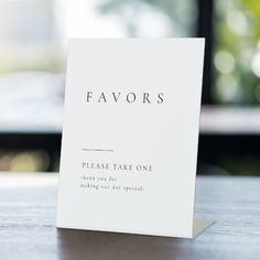 a white card with the words favors on it sitting on a wooden table in front of a window