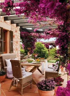 an outdoor dining area with wicker furniture and purple flowers on the arbored patio