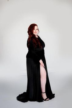 a woman with long red hair wearing a black dress and posing for a photo in front of a white background