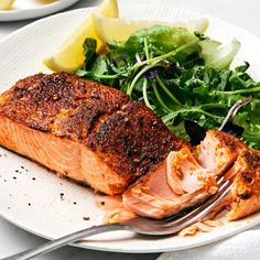 a white plate topped with salmon next to a salad