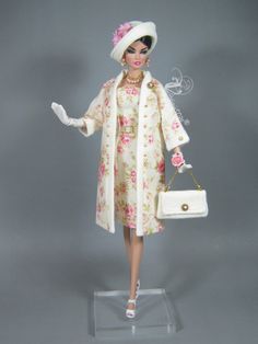 a barbie doll wearing a white coat and pink flowered dress holding a handbag