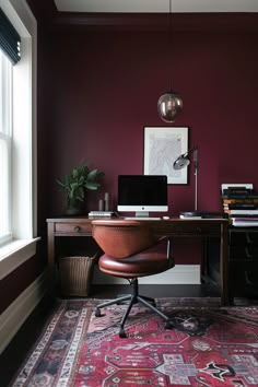 a desk with a computer on top of it in front of a window and a rug