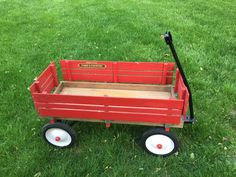 a red wagon sitting on top of a lush green grass covered field with white wheels