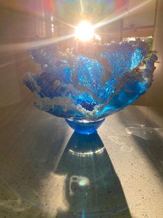 a blue glass bowl sitting on top of a table next to a light shining through the window