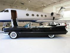 an old black car parked in front of a private jet