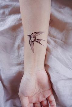 a small hummingbird tattoo on the left inner arm and wrist is shown in black ink