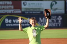 a young boy in a green shirt is holding his baseball glove up to the sky