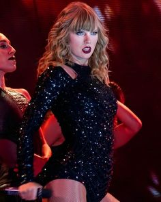 taylor swift performing on stage with her legs spread out in front of her and another woman standing behind her