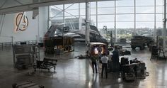 people looking at airplanes in an airplane hanger with many other vehicles on the floor