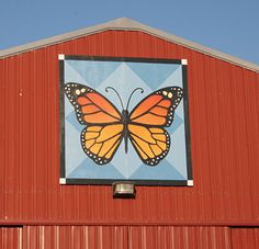 a large orange butterfly painted on the side of a red barn building with blue sky in the background