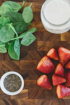 strawberries, spinach leaves and other ingredients on a cutting board next to a glass of milk