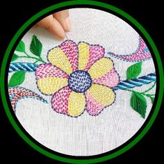 a person is stitching a flower on a white cloth with green and blue trim