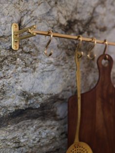 a wooden cutting board sitting next to a stone wall with hooks on it and a cheese grater hanging from the handle