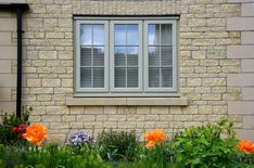 an orange flower is in front of a brick building with two windows and green grass