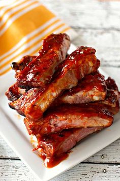 ribs covered in bbq sauce on a white plate next to a yellow and white striped napkin